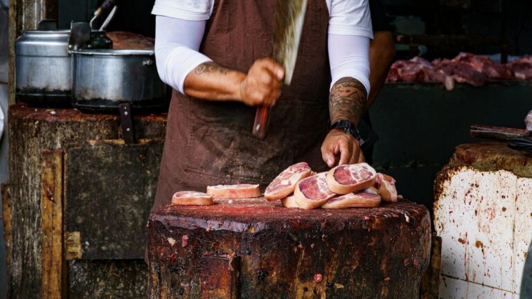 Açougueiro preparando carne em balcão de trabalho.