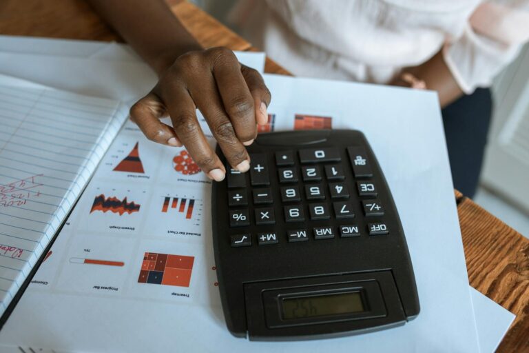 Pessoa usando calculadora sobre documentos financeiros e gráficos