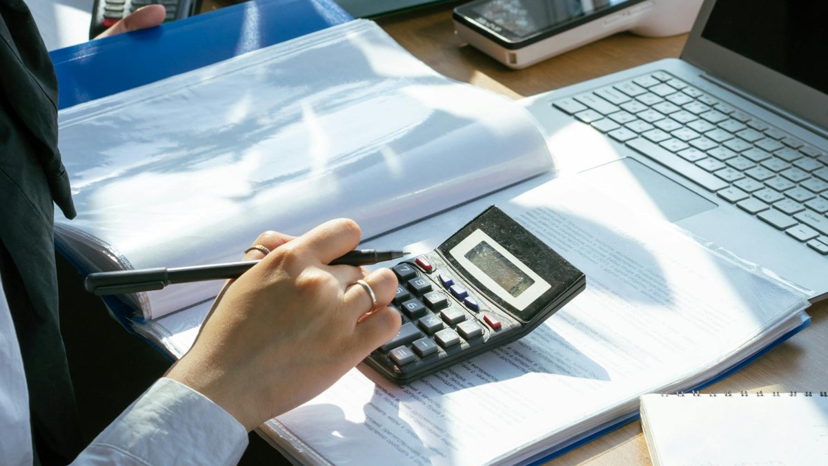Pessoa usando calculadora e notebook para controle financeiro