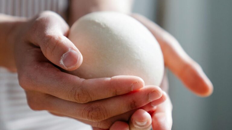 Pessoa preparando massa de pão com as mãos em bancada de panificação.