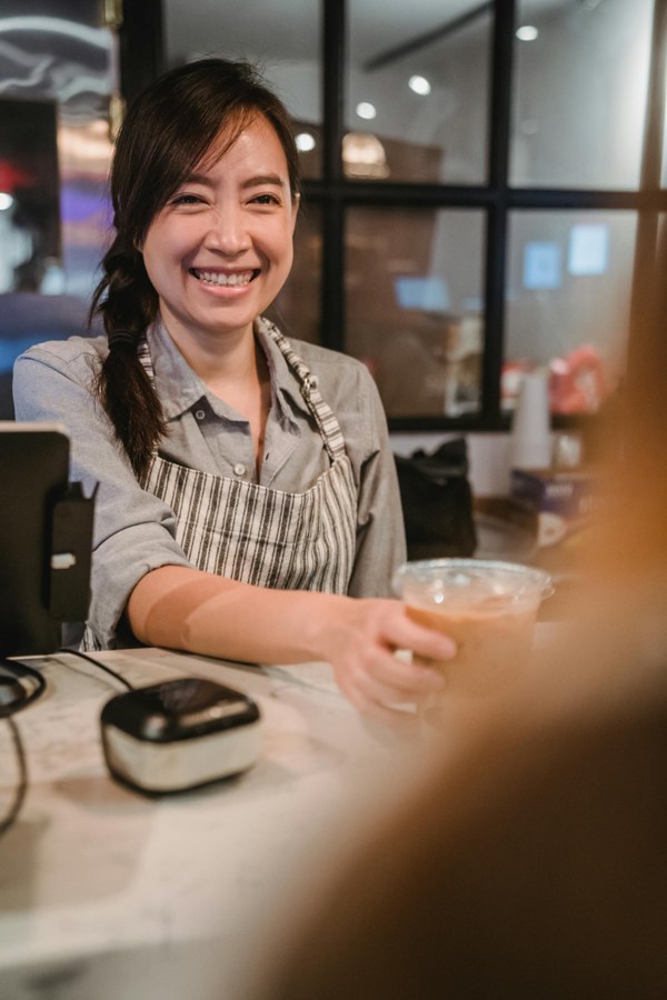 Atendente sorrindo e servindo cliente em pequeno negócio, representando curso de atendimento ao cliente.